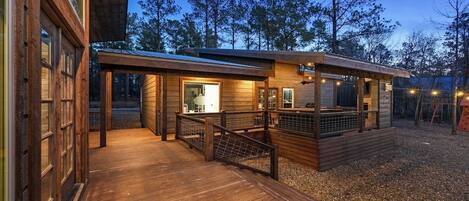 A wooden deck leading to a cabin with a glass door, surrounded by trees.