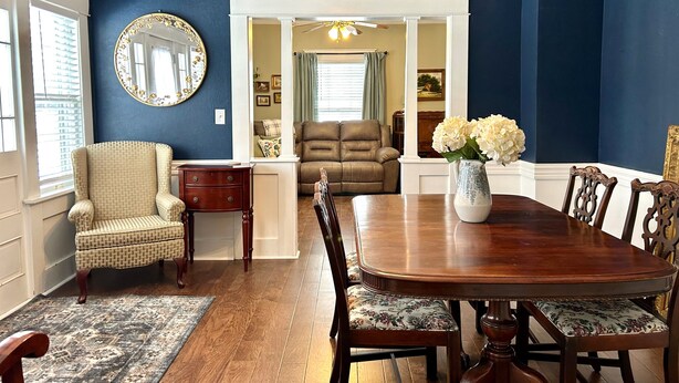 A dining room with a wooden table and chairs, a vase with flowers, and a large mirror on the wall. - Aggie House near ASU (Jonesboro)