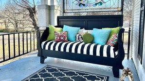 A black and white striped sofa with colorful cushions on a porch with a stained glass window above. - Aggie House near ASU (Jonesboro)