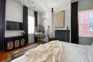 Een slaapkamer met een groot bed, een televisie aan de muur, een stoel en een open haard.