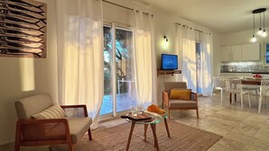 Ein Wohnzimmer mit Sofa, Sessel und Couchtisch, einem Fernseher auf einem Schrank sowie einem Essbereich mit Stühlen und Tisch.