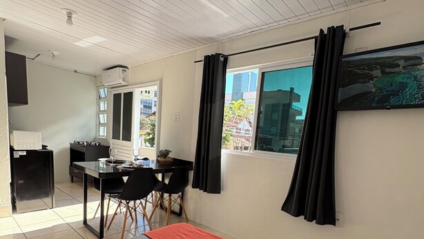 A hotel room with a bed, a desk, a chair, a TV, and a window with curtains. - Loft for couples - Downtown Bombinhas - Near the beach (Bombinhas)