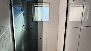 A small bathroom with a toilet, a shower, and a window. - Loft for couples - Downtown Bombinhas - Near the beach (Bombinhas)