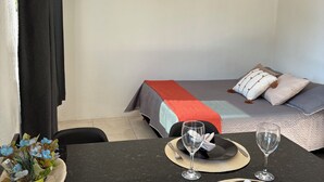 A neatly arranged room with a bed, a dining table set for two, and a small plant on the table. - Loft for couples - Downtown Bombinhas - Near the beach (Bombinhas)
