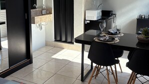 A modern kitchen with a microwave, stove, and black cabinets. There is a dining area with a black table and chairs, and a red and blue rug on the floor. - Loft for couples - Downtown Bombinhas - Near the beach (Bombinhas)