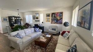 A living room with two white sofas, a coffee table, a striped armchair, and a bookshelf. - Lovely 3-bedroom w/office  beach house in gate-guarded community (Carlsbad)