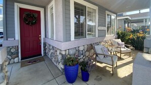 A house with a red door, stone wall, and a porch with a white chair and potted plants. - Lovely 3-bedroom w/office  beach house in gate-guarded community (Carlsbad)
