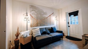 Uma sala de estar moderna com um sofá, um candeeiro fixado na parede e um grande quadro abstrato.