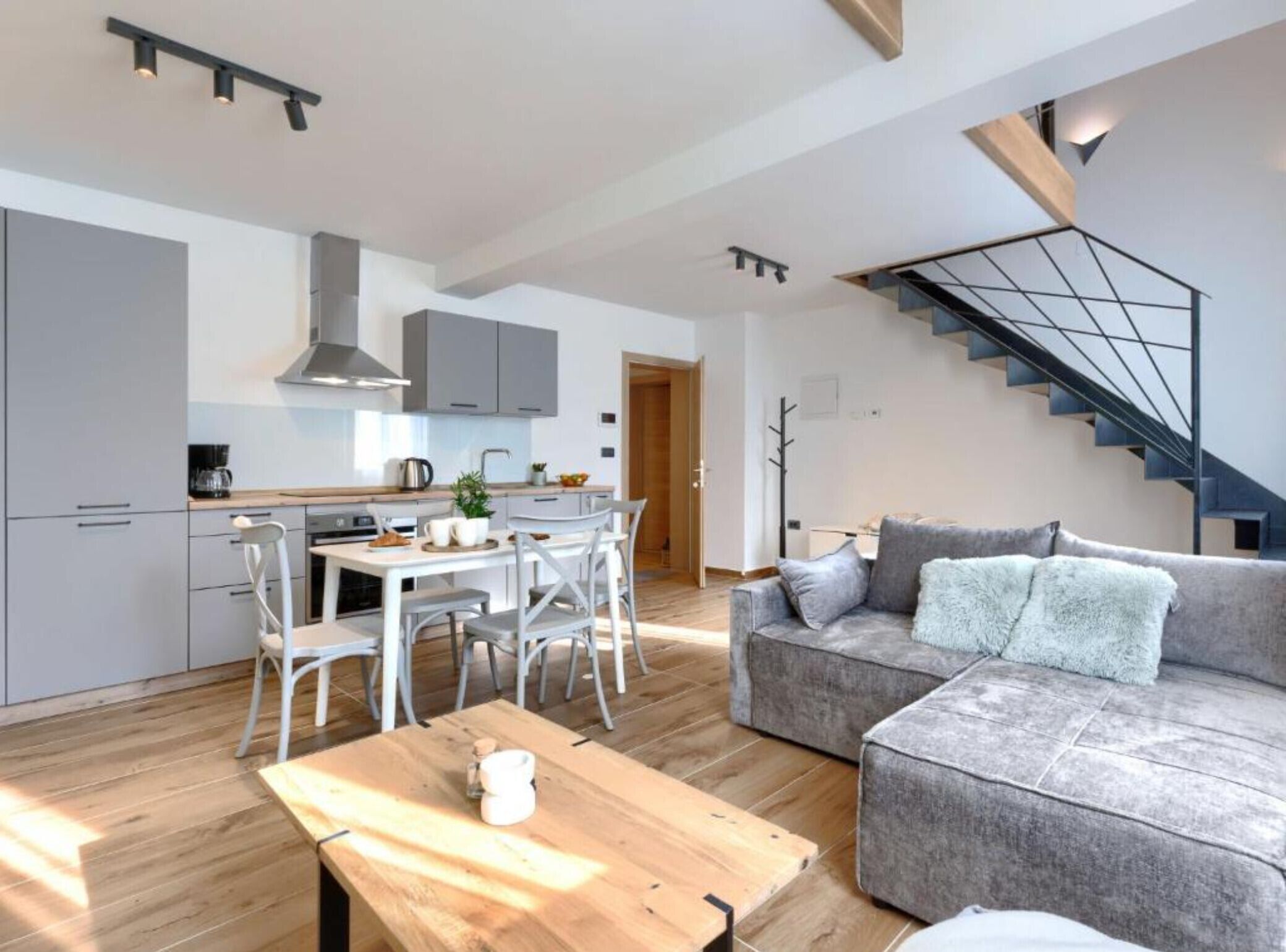 A modern apartment with a kitchen, dining area, and living room. There is a staircase leading to an upper floor.