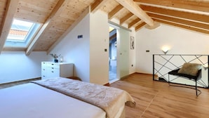Ein Schlafzimmer mit schrägen Wänden, Holzbalken, einem Bett, einem Schminktisch und einem Stuhl.