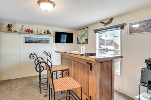 A small, cozy room with a wooden bar counter, two metal chairs, a television mounted on the wall, and a window providing a view of the outside. - Hike, Fish & Unwind: Mtn-View Gem in Cedaredge! (Cedaredge)