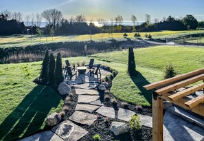 Un patio con suelo de piedra, mobiliario exterior y vistas a un campo verde y árboles.