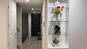 A hallway with a white wardrobe, a black chair, and a glass shelf with decorative items. - SJ House easy access to the Airport and two minutes walking distance to the Mall (Takanini)
