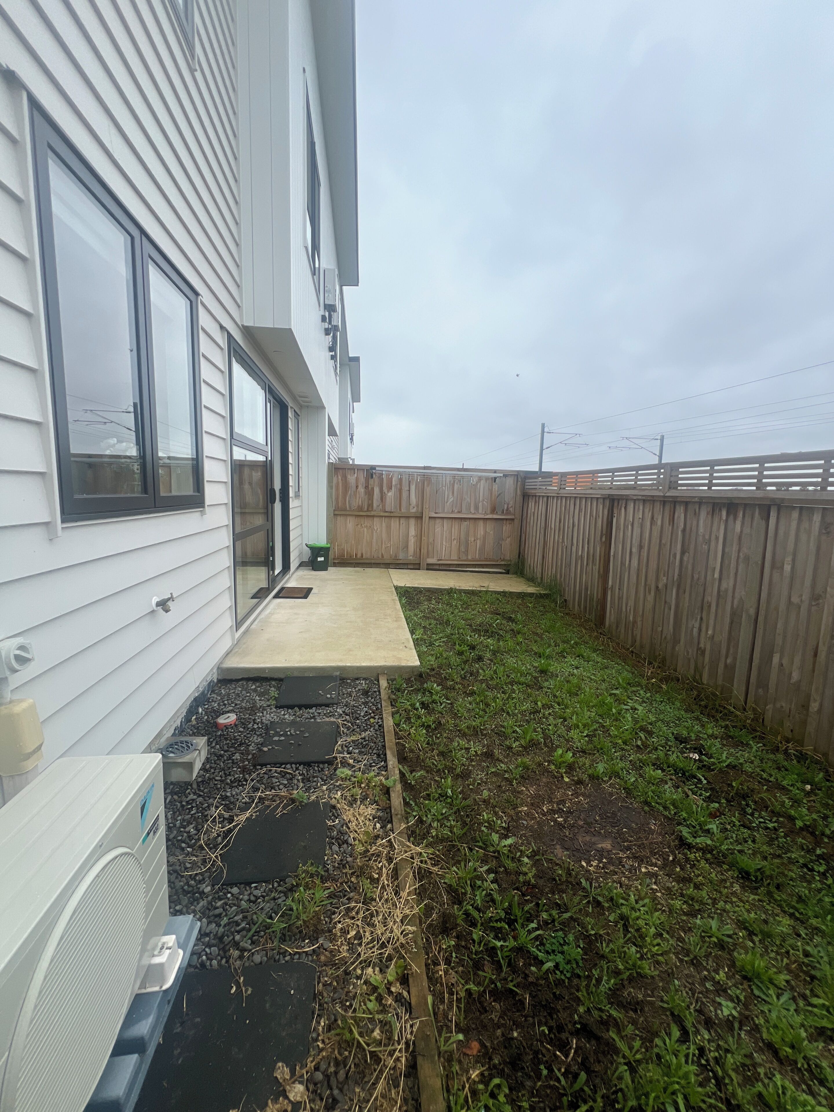 A residential backyard with a wooden fence, a concrete patio, and a small garden area.