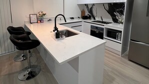 A modern kitchen with a central island, stainless steel appliances, and a minimalist design. - SJ House easy access to the Airport and two minutes walking distance to the Mall (Takanini)