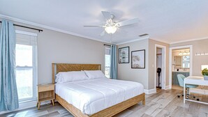 A bedroom with a wooden bed, a ceiling fan, a desk, and a bathroom visible through an open door. - Luxe Heated Pool Oasis, 5 Min to Gulf Beaches, Movie Room (Seminole)