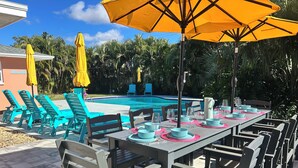A poolside dining area with a pool, lounge chairs, and umbrellas. - Luxe Heated Pool Oasis, 5 Min to Gulf Beaches, Movie Room (Seminole)