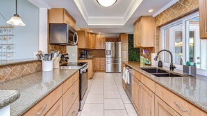 A modern kitchen with granite countertops, stainless steel appliances, wooden cabinets, and a large window providing natural light. - Luxe Heated Pool Oasis, 5 Min to Gulf Beaches, Movie Room (Seminole)