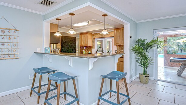 A kitchen with a central island, bar stools, pendant lights, and a potted plant. - Luxe Heated Pool Oasis, 5 Min to Gulf Beaches, Movie Room (Seminole)