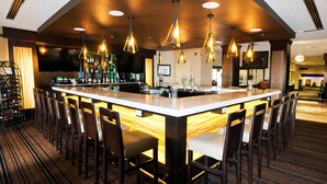 A bar area with a long counter, multiple chairs, and pendant lighting.