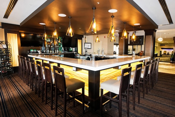 A bar area with a long counter, multiple chairs, and pendant lighting.