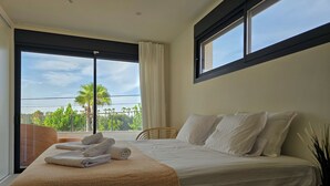 Ein modernes Hotelzimmer mit einem großen Bett, Blick auf Palmen und einem Balkon.