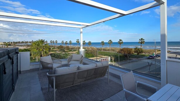 Ein Balkon mit Blick auf den Strand, Korbmöbel und eine Glastür.