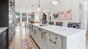 A modern kitchen with a large island, pendant lights, and a view to the living area. - Upscale 3BR Townhome – Walk to Shops & The Monon! (Carmel)