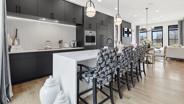 A modern kitchen with dark cabinets, a white island, and bar stools. - Upscale 3BR Townhome – Walk to Shops & The Monon! (Carmel)