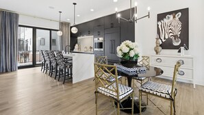 A modern kitchen with dark cabinets, a central island, and a dining area with a round table and chairs. - Upscale 3BR Townhome – Walk to Shops & The Monon! (Carmel)