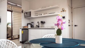 A modern kitchen with white cabinets, a microwave, and a coffee machine. There is a small refrigerator and a sink. A potted plant and a vase with flowers are on the counter. - Cozy Suite in the Heart of Historic Cuenca awaits you (Cuenca)