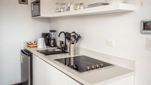 A modern kitchen with white cabinetry, a stainless steel stove, and a built-in oven. There are shelves above the counter holding dishes and glassware. - Cozy Suite in the Heart of Historic Cuenca awaits you (Cuenca)
