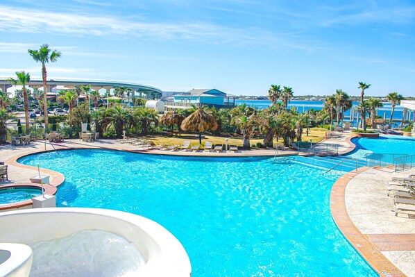 Una gran piscina al aire libre con sillones de descanso y palmeras, rodeada de edificios de un complejo turístico y vistas al océano.