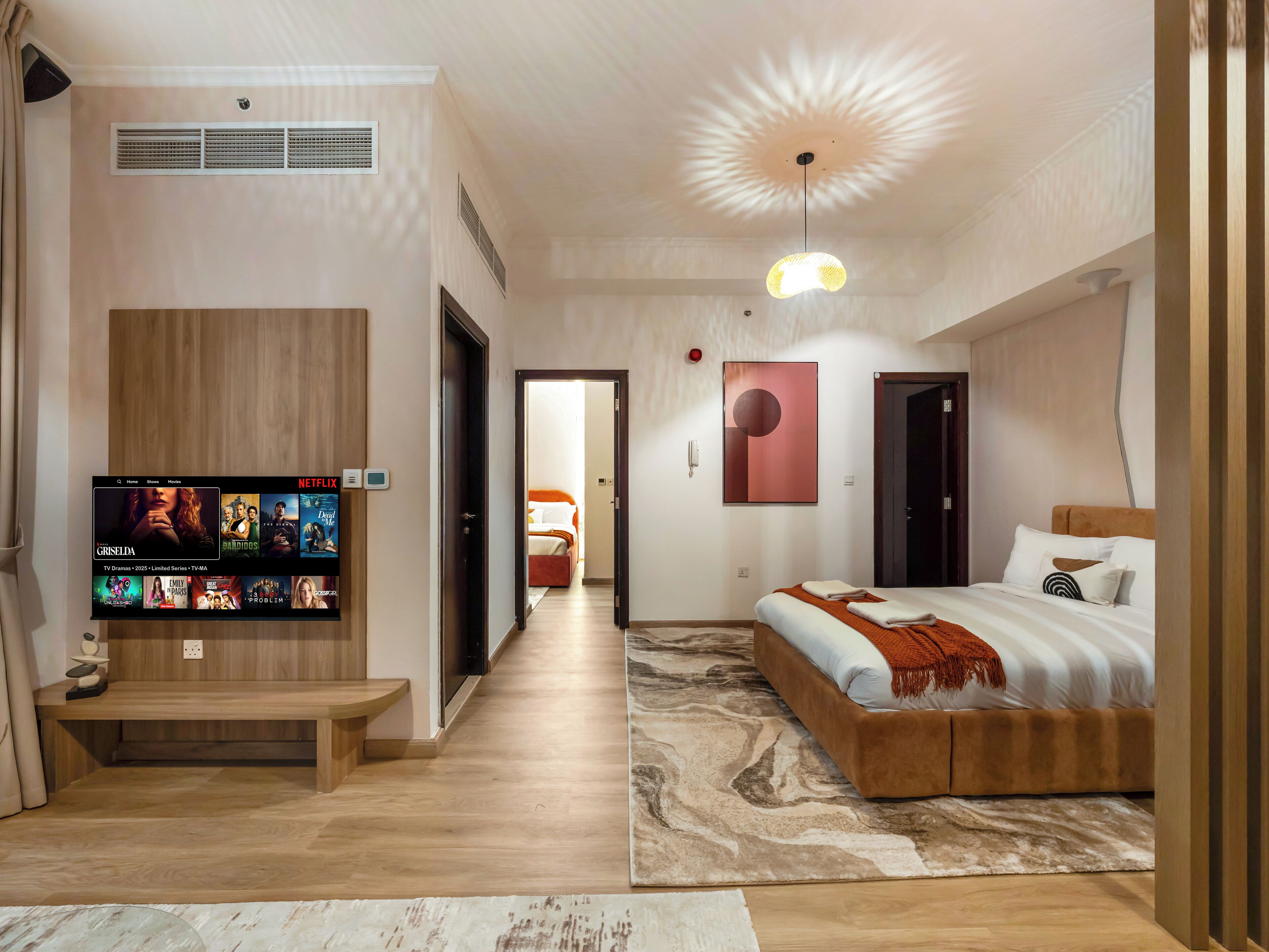 Moderni hotellihuone, jossa on suuri sänky, seinälle asennettu televisio ja käytävä, joka johtaa toiseen huoneeseen.