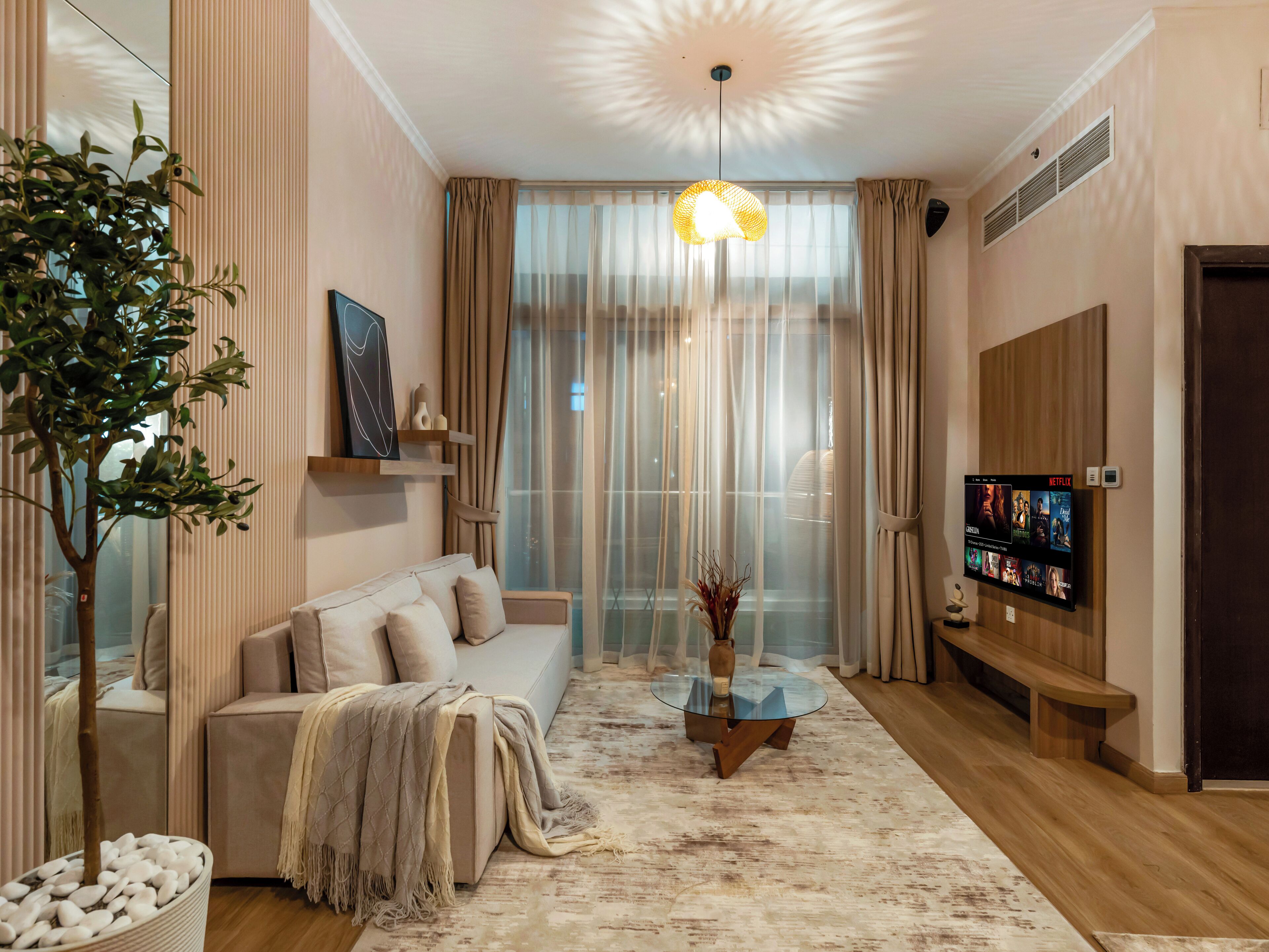 A modern living room with a sofa, a glass coffee table, a TV, and a large window with curtains.