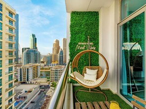 A balcony with a hanging chair, a green wall, and a city view. - Urban Dubai Marina Stay Near Yacht (Dubai)