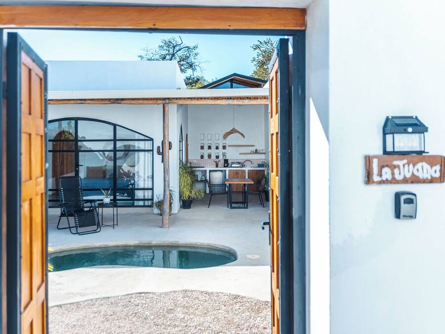 Un umbral abierto que da a una cocina moderna con comedor, piscina y un letrero que dice "La Juana".