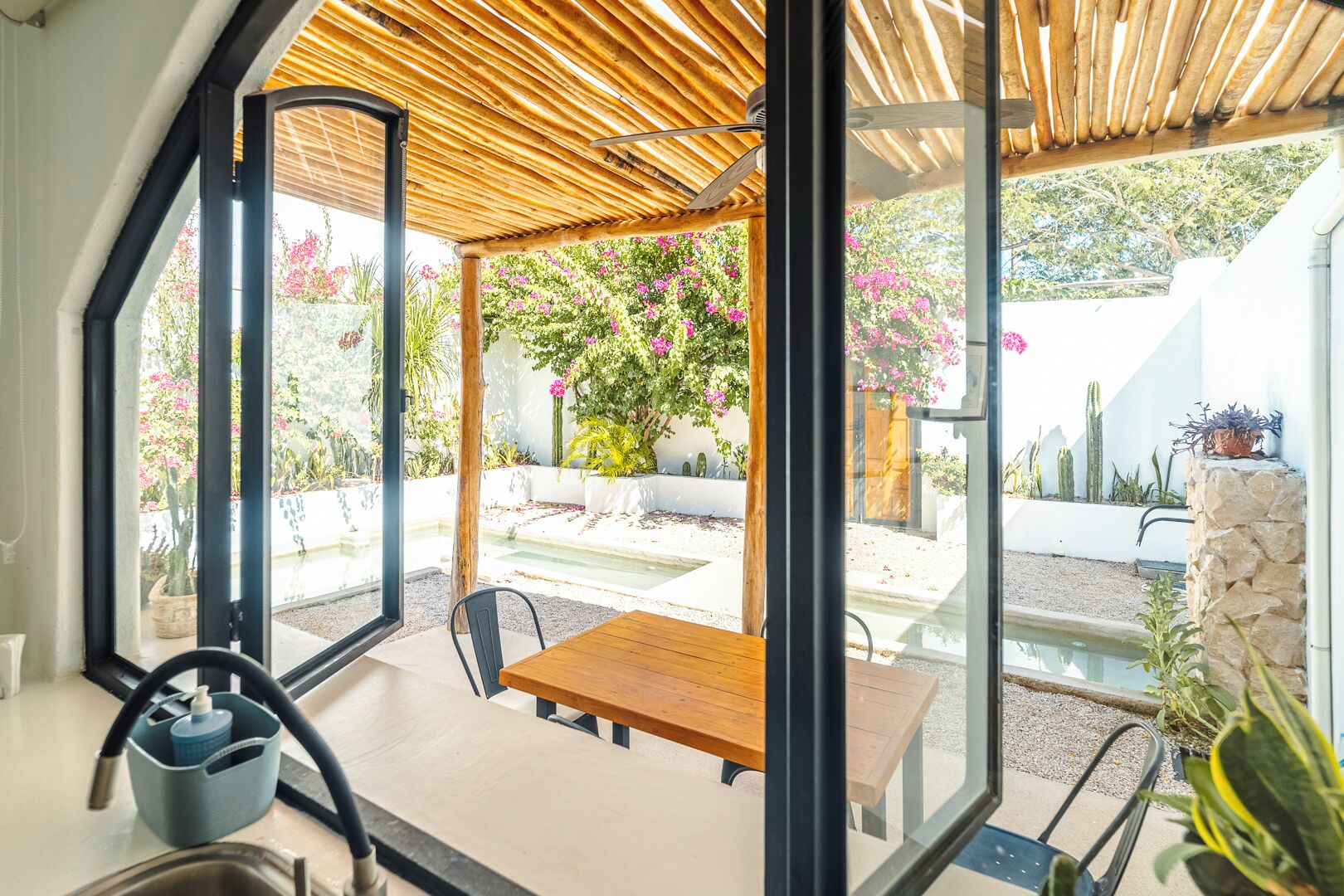Una cocina moderna con una mesa y sillas de madera, horno empotrado y un amplio ventanal con vistas a un jardín con pérgola.
