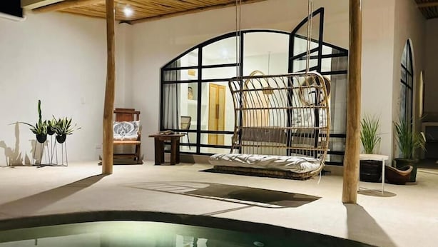 Un espacio exterior moderno con una silla colgante, una piscina y plantas en macetas.