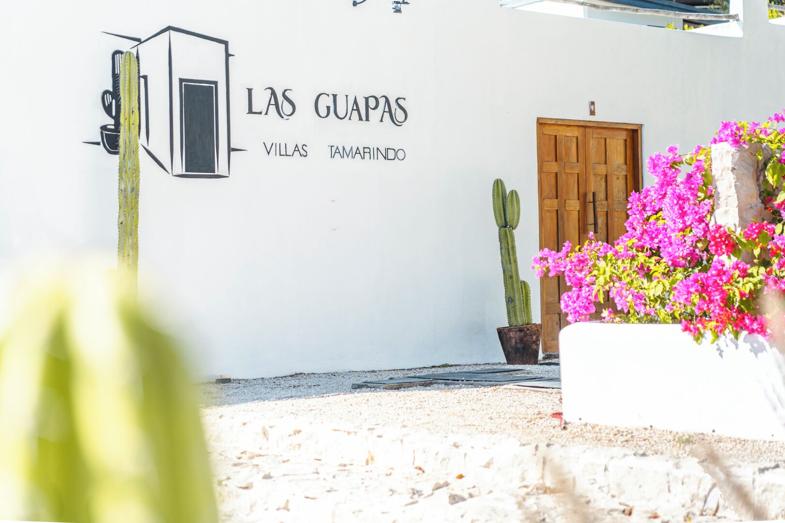 Een witte muur met de tekst 'LAS GUAPAS VILLAS TAMARINDO' en een houten deur.