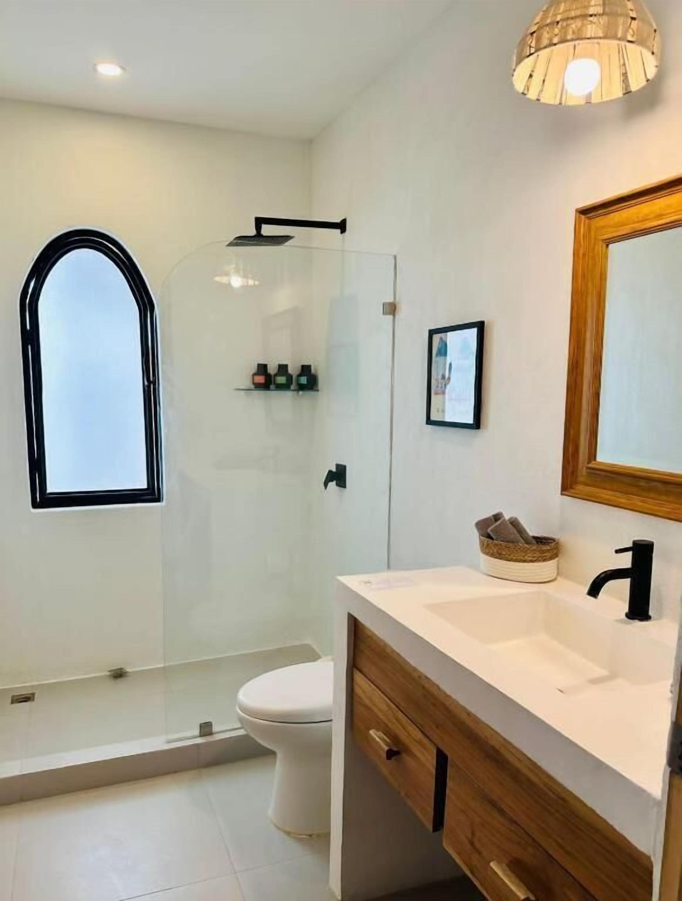 A modern bathroom with a glass shower enclosure, a white toilet, a wooden vanity with a sink, and a large mirror.