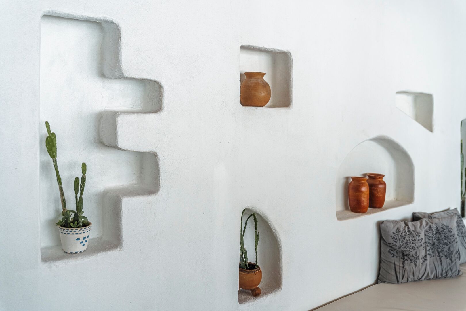 A white wall with geometric cutouts containing potted plants and vases.