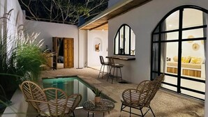 Un patio exterior moderno con piscina, mobiliario de mimbre y zona de comedor con mesa y sillas.