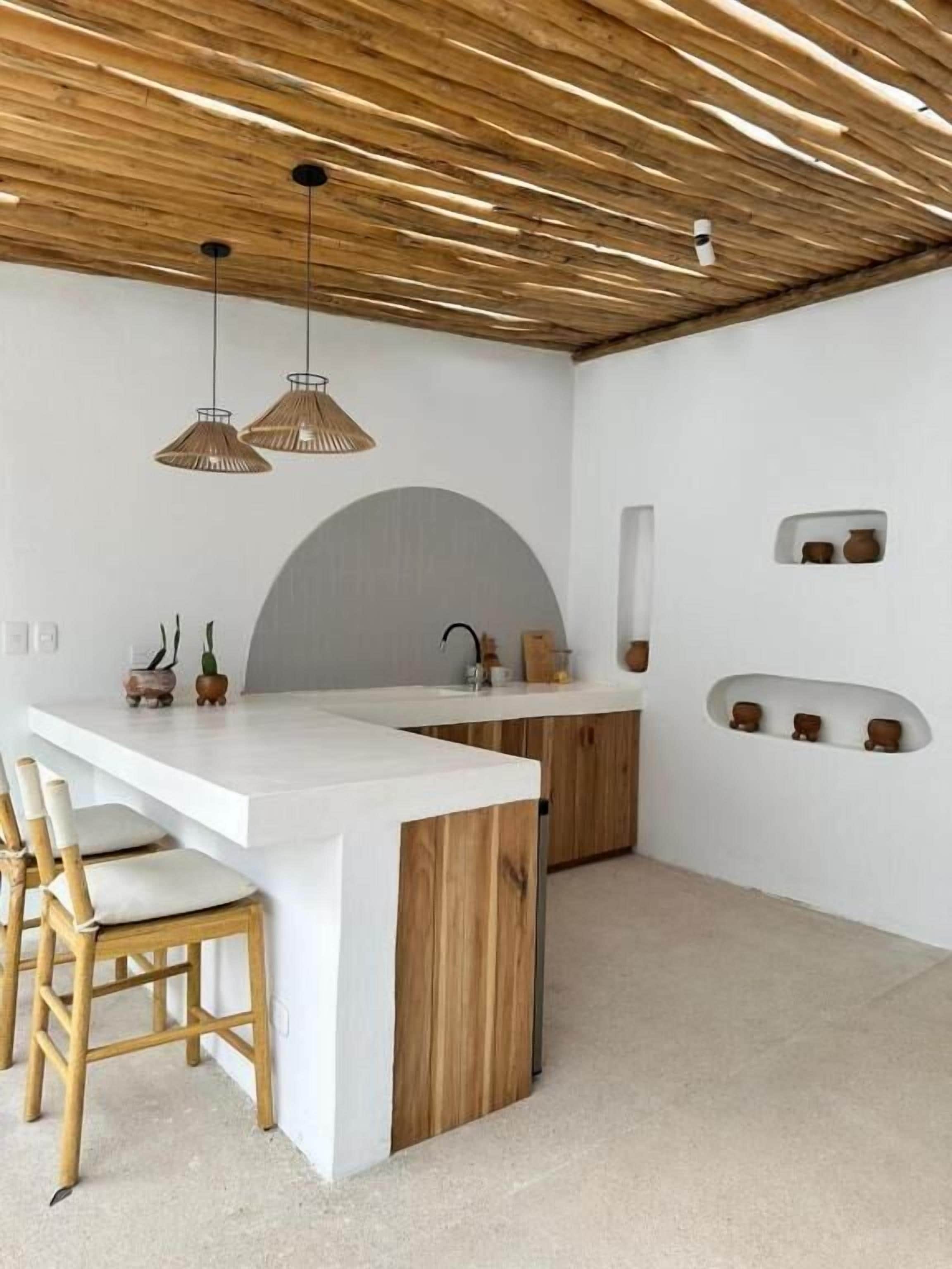 Una cocina moderna con una isla blanca, techo de madera y luces colgantes.