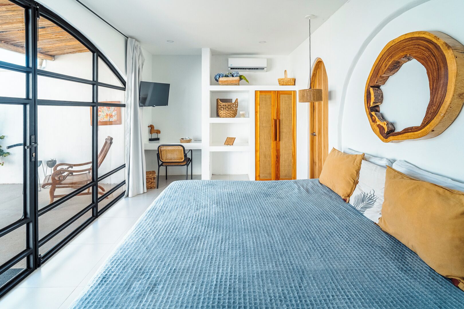 Una camera da letto con un letto grande, un armadio in legno, una televisione e un balcone con una sedia.