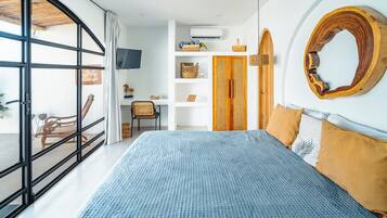 Una camera da letto con un letto grande, un armadio in legno, una televisione e un balcone con una sedia.