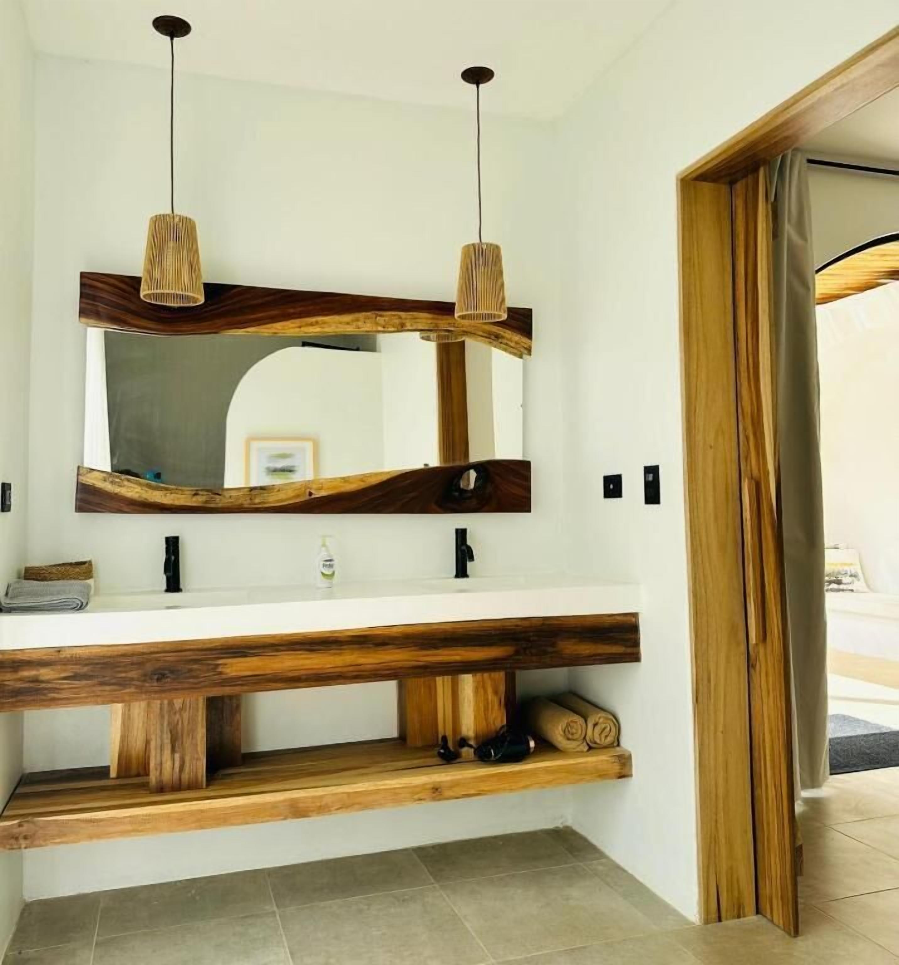 A bathroom with a wooden vanity, two pendant lights, and a mirror with a wooden frame.
