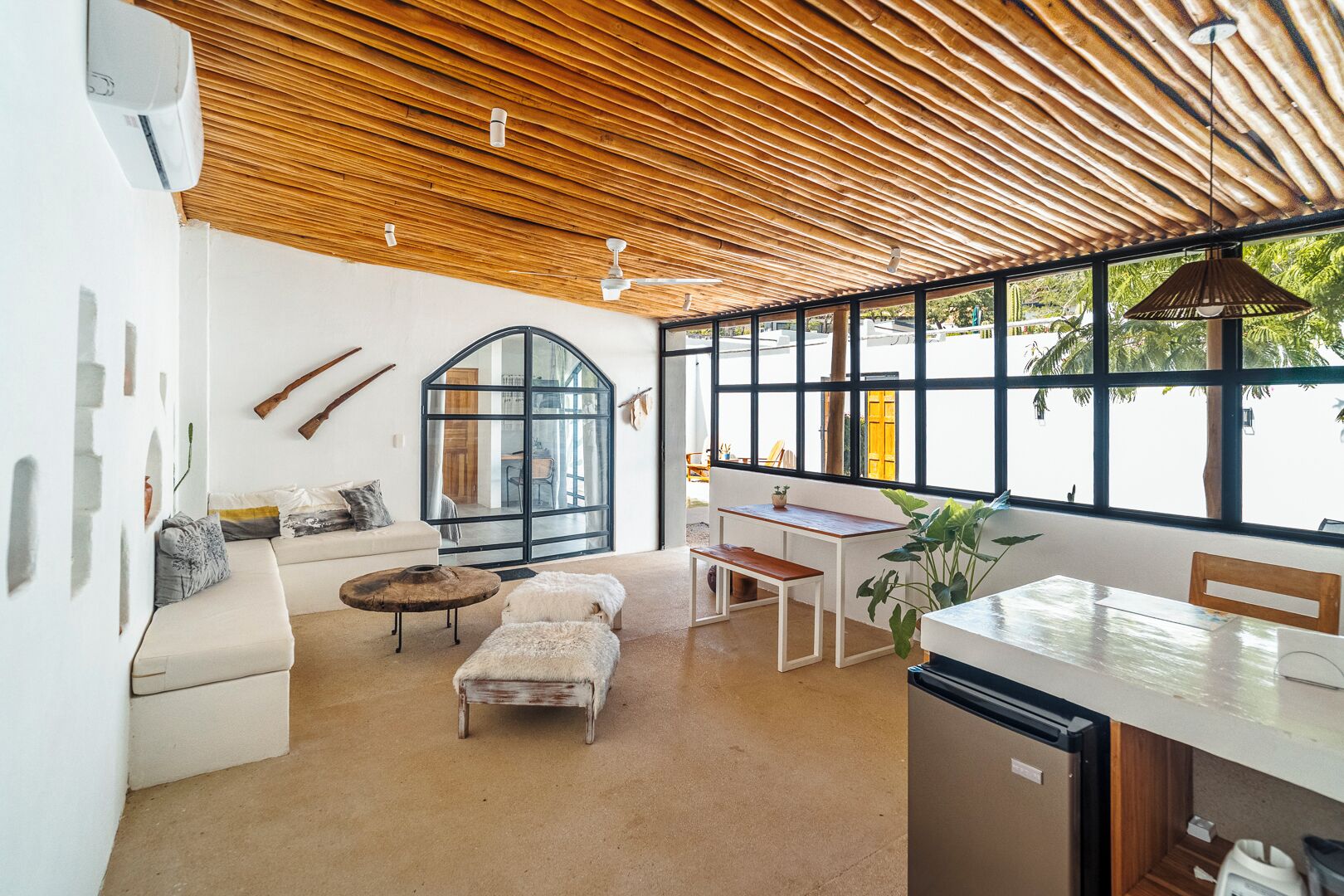 Interior moderno com teto de madeira, uma grande janela em arco, área de refeições e cozinha.