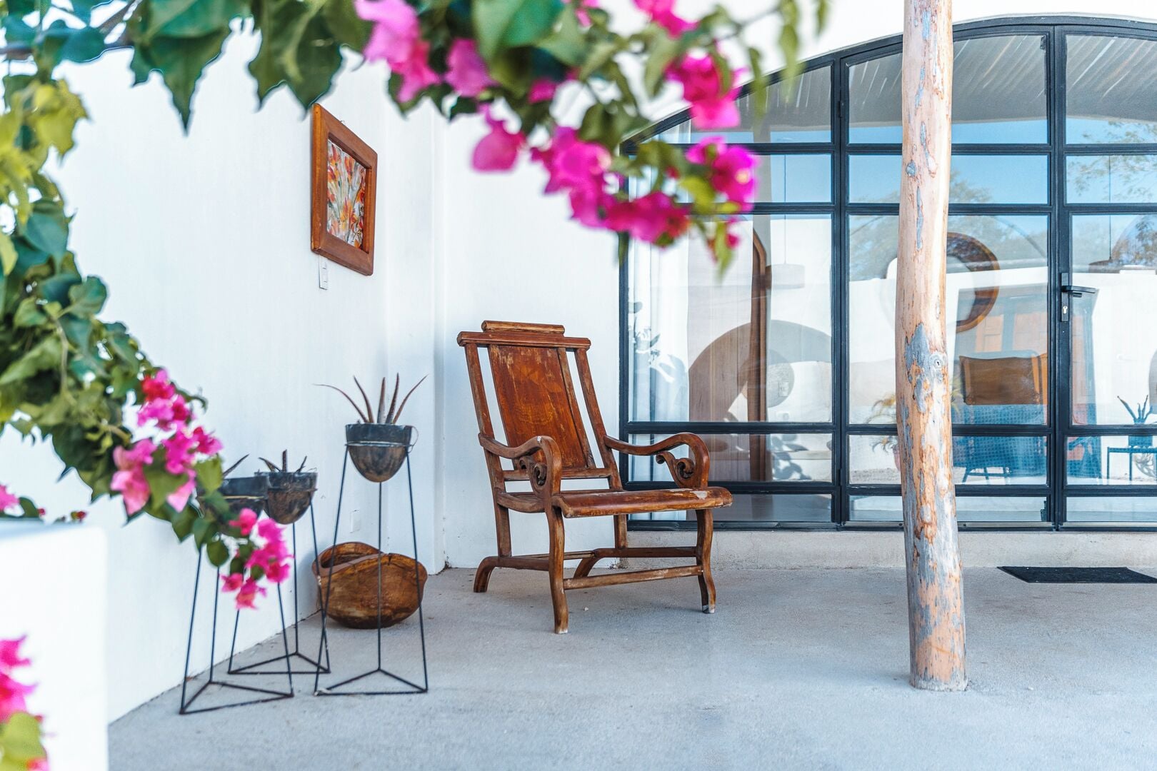 A wooden chair in a covered outdoor area with potted plants and a glass wall.