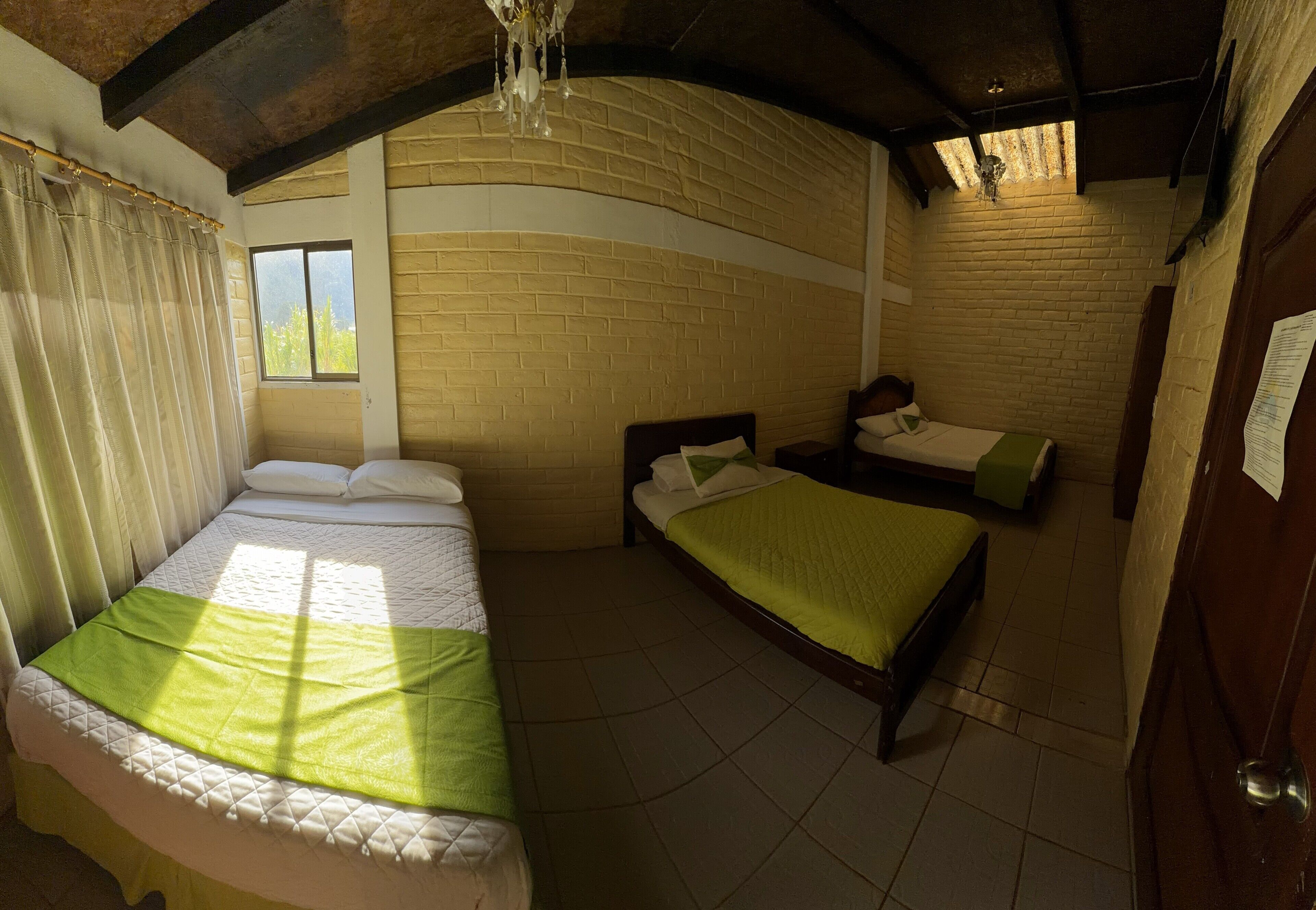 Ein Zimmer mit einem großen Bett, einem kleineren Bett, einem Fenster und einer Ziegelwand.